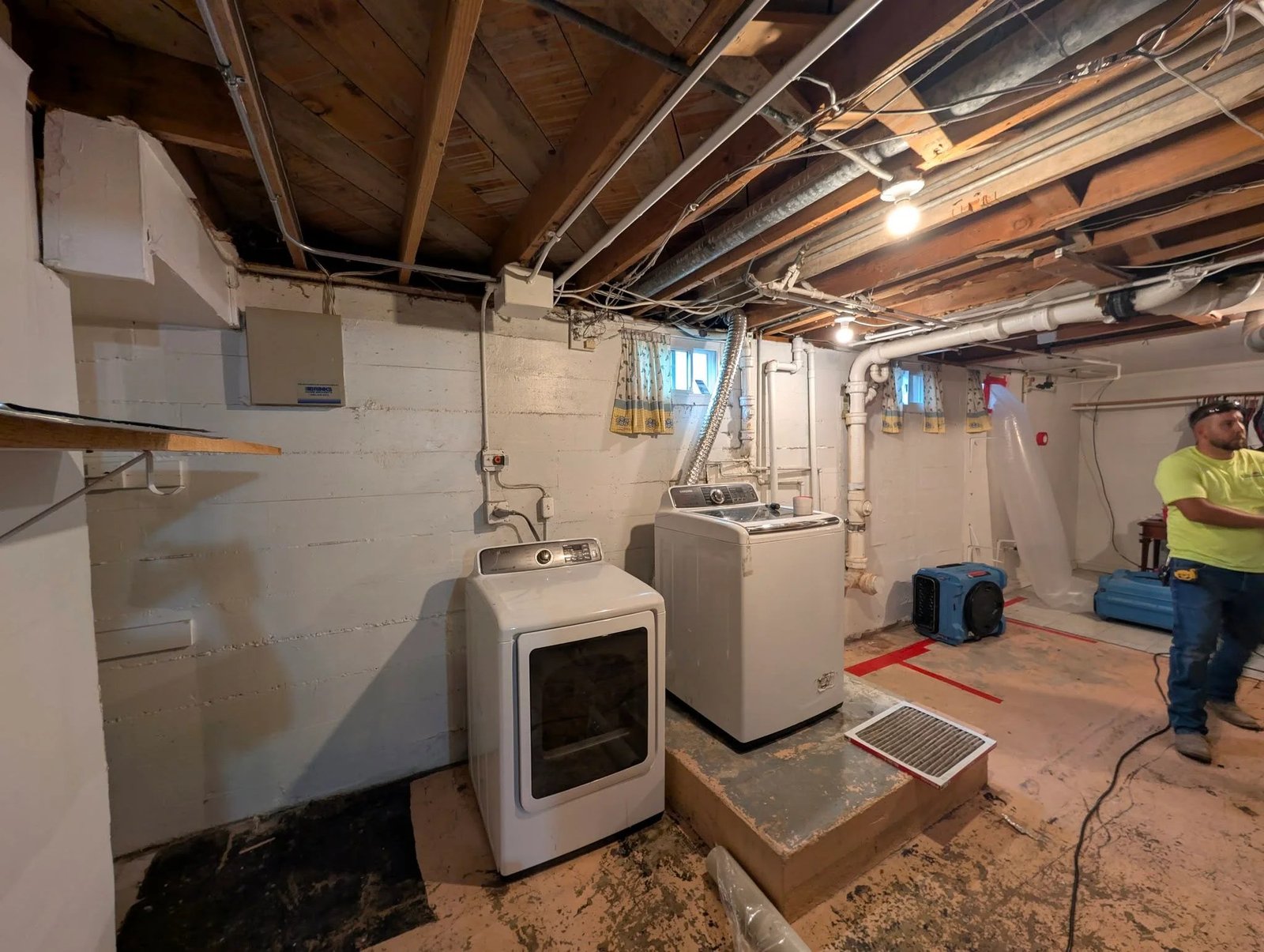 A technician on site with drying equipment set up in a basement laundry area