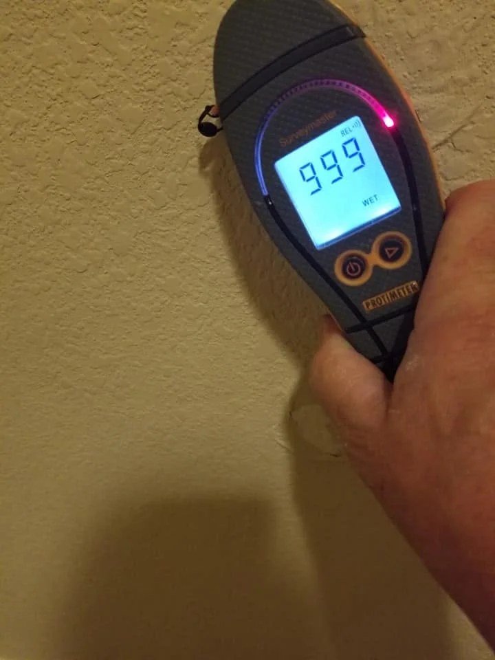 Moisture meter held against a wall showing a saturated reading